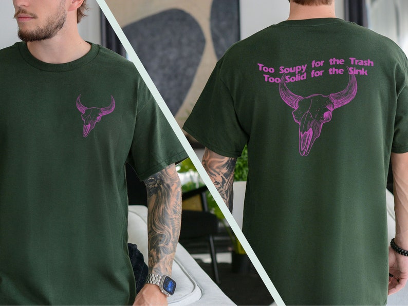 May include: A dark green t-shirt with a pink bull skull graphic on the front and the text "Too Soupy for the Trash Too Solid for the Sink" on the back.