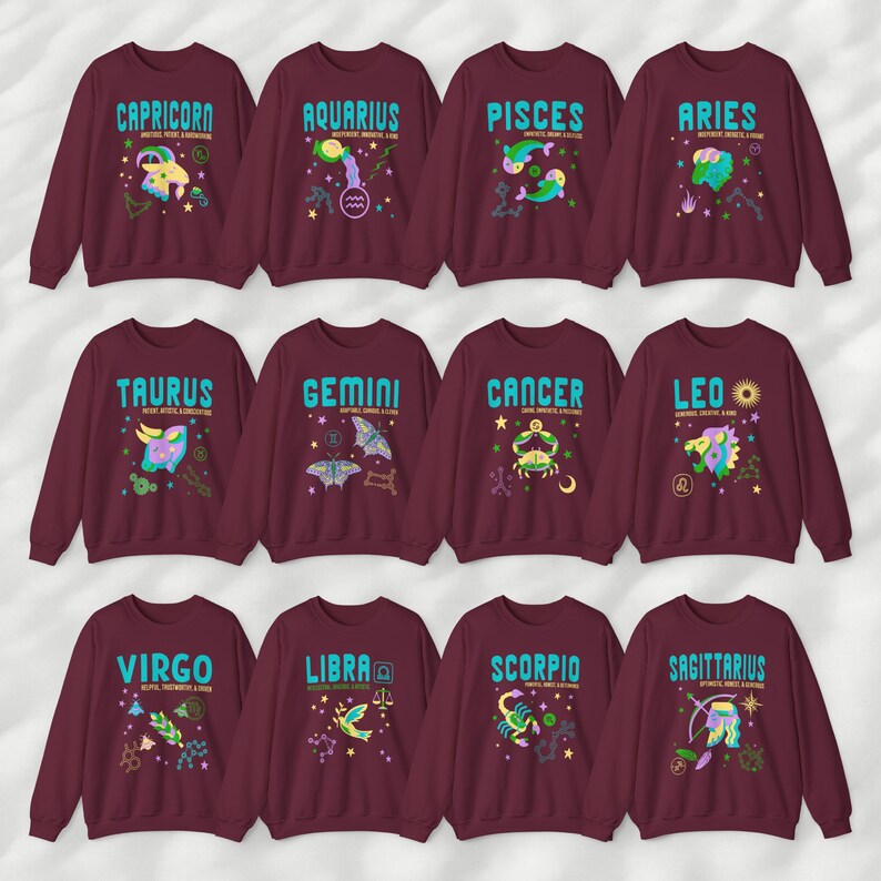 May include: Twelve maroon sweatshirts with a different zodiac sign on each. The signs are Capricorn, Aquarius, Pisces, Aries, Taurus, Gemini, Cancer, Leo, Virgo, Libra, Scorpio, and Sagittarius. Each sign is depicted with a colorful illustration and the name of the sign in blue text.