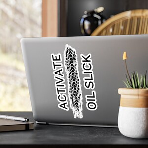 May include: A white laptop sticker with black text that reads "Activate Oil Slick" and a black tire tread print graphic.