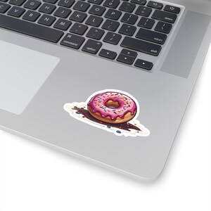 May include: A pink frosted donut with colorful sprinkles on top. The donut is sitting on a brown surface with more sprinkles scattered around it.