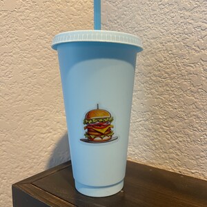 May include: A light blue reusable cup with a straw and a sticker of a hamburger on the front.