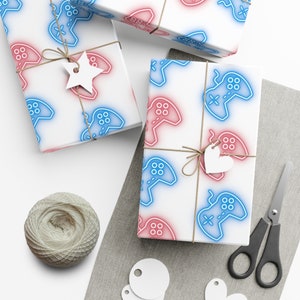 May include: White gift wrap with a repeating pattern of blue and red video game controllers. The controllers have a neon glow effect. The wrap is tied with twine and decorated with a white star and heart.