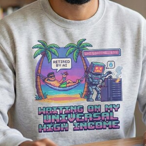 以下が含まれることがあります： 「Retired by AI」と「Waiting on my Universal High Income」と書かれたカラフルなグラフィックが特徴のライトグレーのスウェットシャツ。ハンモックでくつろぐ人とロボットが描かれています。男性が笑顔で、ノートパソコンのある机に座っています。