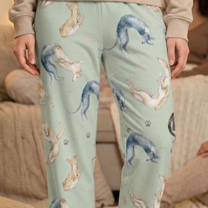 May include: Light green pajama pants with a repeating pattern of watercolor greyhounds in various poses. The pants also feature small paw prints and star-like shapes. The pants are made of a soft, comfortable material.