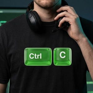 May include: Black t-shirt with a green Ctrl+C graphic. The design features two green, translucent keycaps with the text "Ctrl" and "C" in white. The person in the image is wearing a headset.