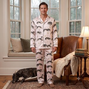 May include: A light pink pajama set consisting of a long-sleeved button-down shirt and matching trousers. The fabric features a repeating pattern of black and white dogs in various resting positions, interspersed with small gold stars and moon shapes.