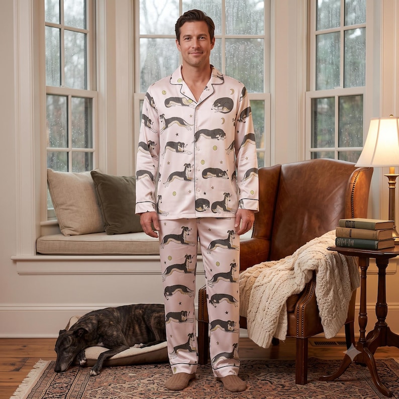 May include: A light pink pajama set consisting of a long-sleeved button-down shirt and matching trousers. The fabric features a repeating pattern of black and white dogs in various resting positions, interspersed with small gold stars and moon shapes.