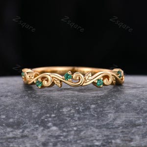 May include: A delicate gold band ring featuring a vine design and small green gemstones. The ring is a simple and elegant piece of jewellery.
