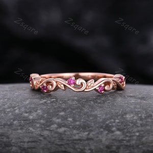 May include: A delicate rose gold band ring with a floral design and pink gemstones. The ring features a swirling vine pattern with leaves and small pink stones.
