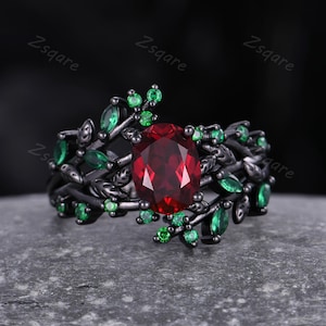 May include: Black ring with a large red gemstone surrounded by smaller green gemstones. The ring features a delicate, leafy design.