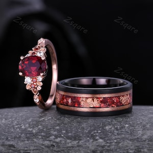 Peut inclure: Un ensemble de deux alliances. La bague de fiançailles présente une grande pierre rouge de forme ovale entourée de petites pierres blanches et rouges. La bague de mariage est noire avec une incrustation rouge et or.