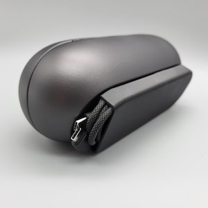 Puede incluir: Un ratón de ordenador ergonómico gris oscuro con una parte superior redondeada y un lado rectangular. Un cable USB negro trenzado con un conector USB-A está conectado. El ratón está diseñado para la comodidad y la eficiencia.