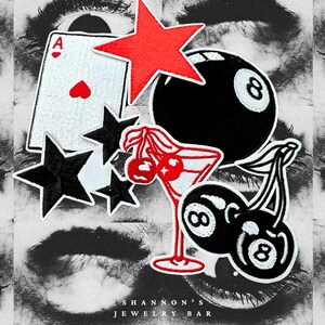 May include: A collection of embroidered patches featuring a red star, black stars, an Ace of Hearts playing card, a black eight ball, a martini glass with cherries, and a pair of cherries with an eight ball. The text "SHANNON'S JEWELRY BAR" is at the bottom.