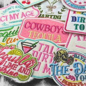 May include: A collection of embroidered patches with various designs and text. The patches feature phrases like "Cowboy Tequila," "Talk Dirty to Me," and "Tequila Lime and Shine." Colors include pink, green, yellow, and blue, with a mix of fonts and illustrations.