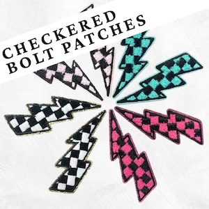 Op de afbeelding: Een verzameling geborduurde bliksemflits patches in diverse kleuren, waaronder zwart-wit, roze en teal, met een geblokt patroon. De patches zijn in een cirkelvorm gerangschikt. De tekst "CHECKERED BOLT PATCHES" staat bovenaan.