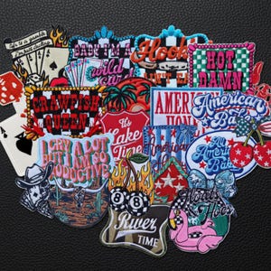 Puede incluir: Una colección de parches bordados con varios diseños y texto. Los parches presentan frases como "Baby I'm a Wild Card", "Hot Damn" y "Crawfish Queen". Otros diseños incluyen naipes, cerezas y un flamenco.