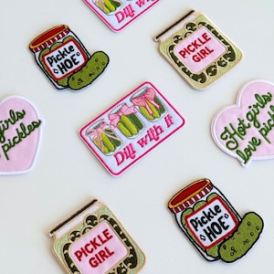 Könnte beinhalten: Eine Sammlung von gestickten Aufnähern mit Designs zum Thema Essiggurken. Die Aufnäher zeigen Gläser mit Essiggurken, Texte wie "Pickle Girl" und "Pickle Hoe" sowie Sätze wie "Dill with it" und "Hot girls love pickles". Die Aufnäher sind in Rosa, Grün und Weiß gehalten.