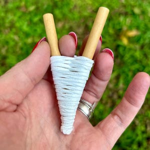 May include: White string wrapped around two wooden sticks to form a cone shape.