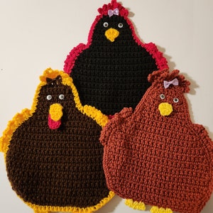 May include: Three crocheted chicken pot holders. One is black with a red trim, one is brown with a yellow trim, and one is red with a yellow trim. Each chicken has a yellow beak, black eyes, and a purple bow.