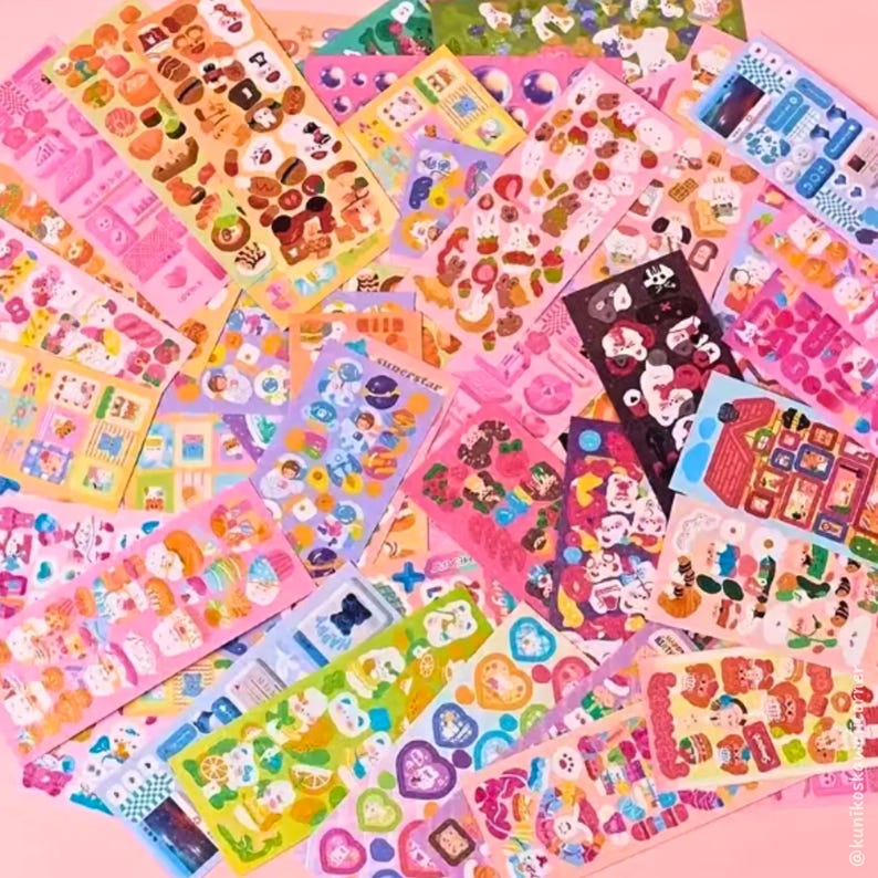 Op de afbeelding: Een verzameling kleurrijke sticker vellen met diverse ontwerpen, waaronder voedsel, dieren en harten. De stickers zijn in roze, gele, blauwe en groene tinten. Sommige vellen bevatten tekst, zoals "sunnerstar".