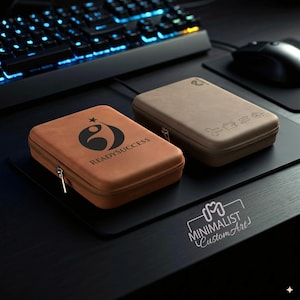 May include: Two rectangular zippered cases. One is tan with the text "READYSUCCESS" and a logo. The other is brown with etched icons. Both cases are on a black surface near a keyboard and mouse.