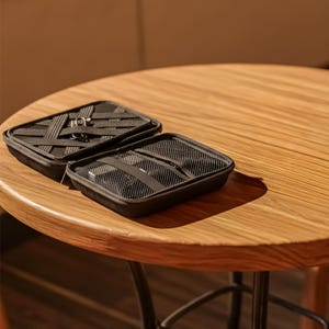 Open black tech case with elastic straps and zippered mesh pouches, sitting on a round wooden table.