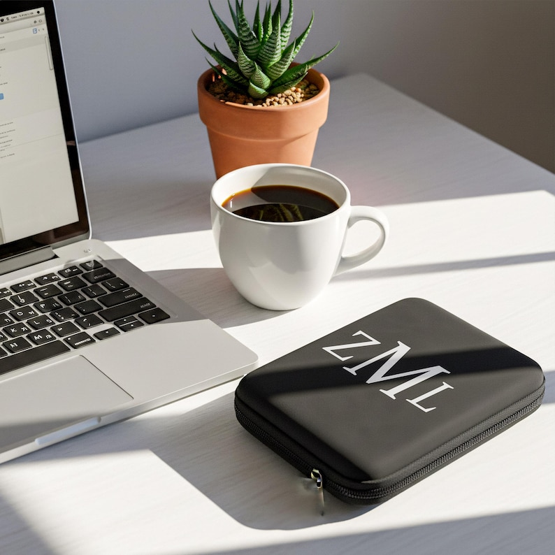 Desk setup with a laptop, a white coffee mug, a small potted succulent, and a black personalized leatherette case with white lettering reading ZML.