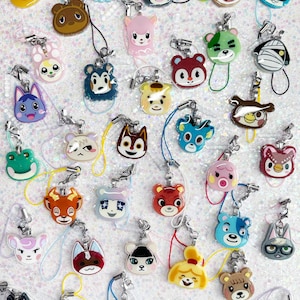 May include: A collection of colorful character charms, each with a unique animal face design. The charms are attached to silver keychains with matching colored lanyards. The charms are made of a glossy material and are arranged on a sparkly white surface.