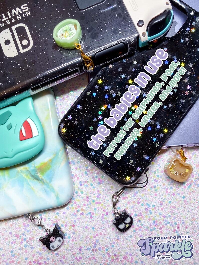 Puede incluir: Funda de tel&eacute;fono negra con un patr&oacute;n de estrellas brillantes y el texto "the babies in use". Incluye colgantes de un rollo de sushi, un oso y un gato negro. Tambi&eacute;n incluye una Nintendo Switch y una funda Bulbasaur.