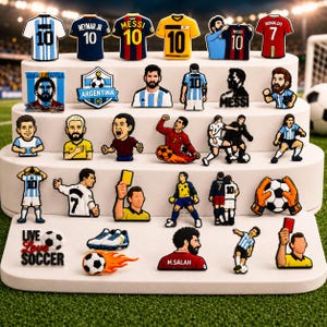 May include: A collection of soccer-themed shoe charms featuring various professional players, team jerseys, referees, and soccer balls. The charms display figures in diverse poses, including holding yellow and red cards, dribbling, and celebrating goals.