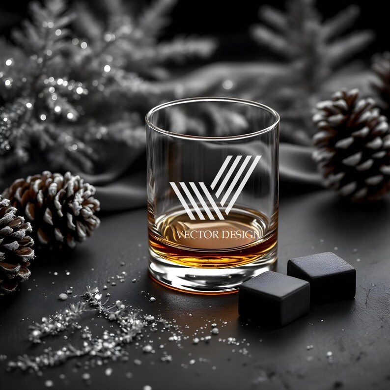 May include: A clear glass whiskey tumbler with a geometric design etched on the side. The glass is filled with amber liquid and sits on a black surface with two black ice cubes.