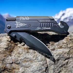 May include: A black multi-tool with a silver inscription that reads "David 01/01/2025 Love, Amanda". The tool has a blade, a seatbelt cutter, and a glass breaker.