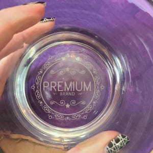 May include: A clear glass cup with a purple background. The cup has a decorative design with the words "Premium Brand" in the center.