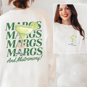 May include: White sweatshirt with green text that reads "MARGS MARGS MARGS MARGS And Matrimony!" and a green illustration of a margarita glass with a lime wedge. The back of the sweatshirt has a small green illustration of a margarita glass with the text "That's the Spirit!"