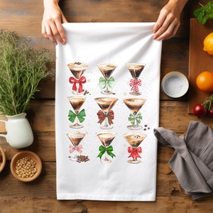 May include: White kitchen towel with a design of nine coffee cocktails decorated with red and green bows. The cocktails are in martini glasses and have a brown liquid inside.