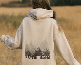 May include: A beige hoodie with a forest silhouette and the text "Leave the Road" printed on the back. The hoodie is worn by a person standing in a field.