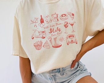 May include: A white t-shirt with a red graphic design featuring Italian icons like a Vespa scooter, pizza, pasta, and a glass of wine. The text "With Love From, Italy Ciao, Ciao!" is printed on the shirt.