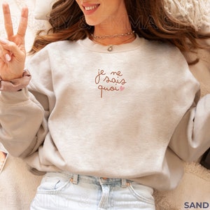May include: A light grey sweatshirt with the French phrase "Je ne sais quoi" in brown script with a small pink heart.