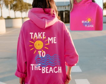 May include: Pink hoodie with the text "Take me to the beach" in white and blue lettering. A yellow sun and blue waves are depicted on the hoodie. The back of the hoodie has the text "Beach Please" in white lettering with a yellow sun and blue waves.