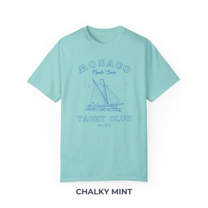 Peut inclure: Un t-shirt bleu clair avec un graphique repr&eacute;sentant un voilier et le texte "MONACO Monte Carlo YACHT CLUB Est. 1953".