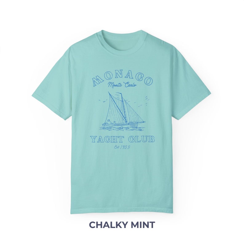 Peut inclure: Un t-shirt bleu clair avec un graphique repr&eacute;sentant un voilier et le texte "MONACO Monte Carlo YACHT CLUB Est. 1953".