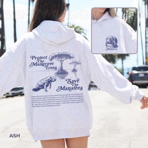 May include: A gray hooded sweatshirt with a blue graphic print on the back. The graphic features a manatee swimming near mangrove trees and the text "Protect The Mangrove Trees" and "Save The Manatees".