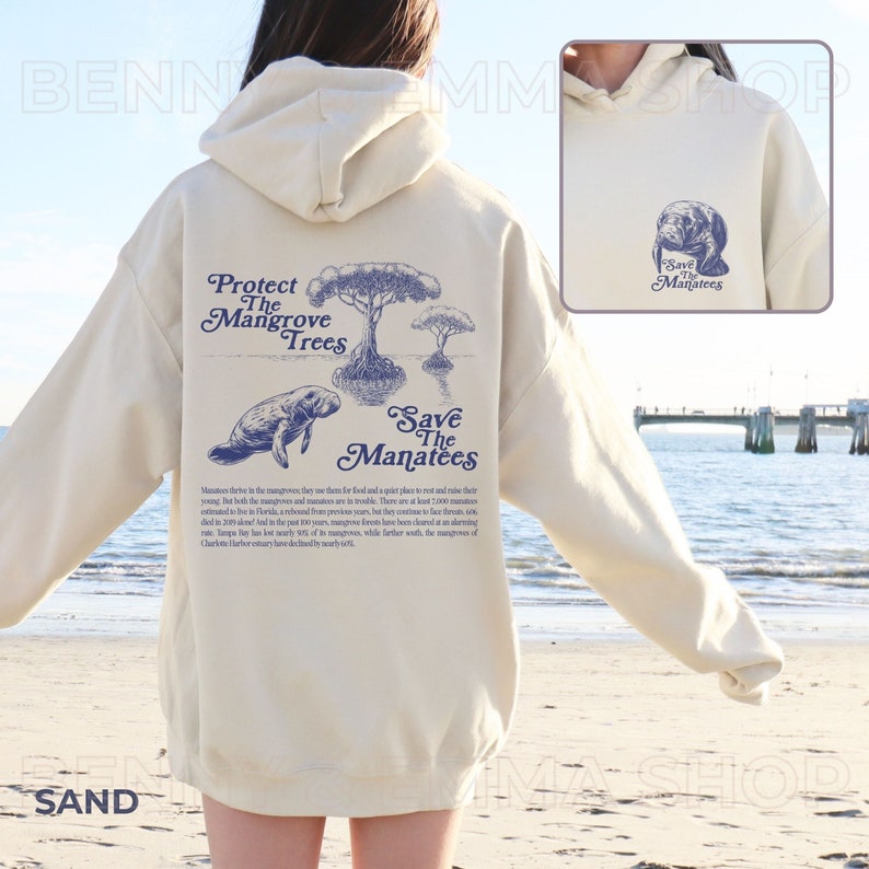 May include: A cream-colored hoodie with a blue illustration of a manatee swimming near mangrove trees. The text "Protect the Mangrove Trees" and "Save the Manatees" is printed on the back of the hoodie. The text "Save the Manatees" is also printed on the front of the hoodie with a smaller illustration of a manatee.