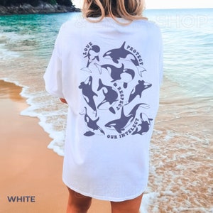 May include: White t-shirt with a graphic of orcas and the text "Love, Protect & Respect Our Intellect" printed on the back.