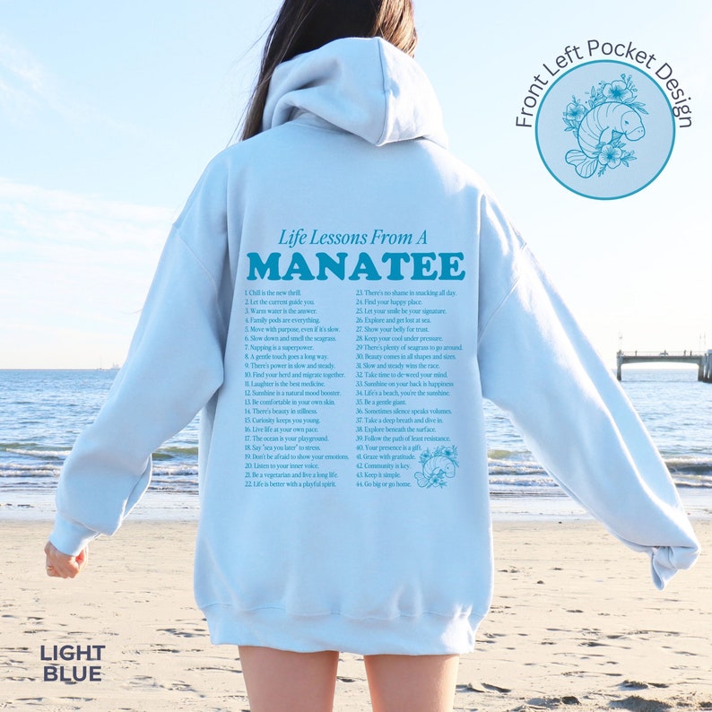 K&ouml;nnte beinhalten: Hellblauer Kapuzenpullover mit einem grafischen Aufdruck eines Seekuhs und dem Text "Life Lessons From A Manatee" mit einer Liste von 44 Lebenslektionen. Der Pullover hat eine linke Brusttasche mit einem grafischen Aufdruck eines Seekuhs.