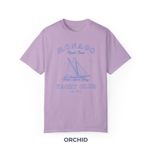 Peut inclure: Un t-shirt lavande avec un graphique bleu d'un voilier et le texte "MONACO Monte Carlo YACHT CLUB Est 1953"