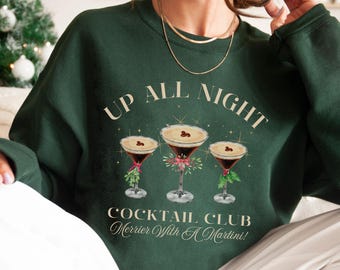 Può includere: Una felpa verde con il testo "Up All Night Cocktail Club Merrier With A Martini!" e una grafica di tre bicchieri da martini con bacche rosse e foglie verdi.