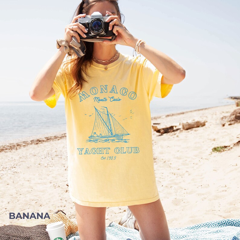 Peut inclure: T-shirt jaune avec un graphique bleu d'un voilier et le texte "MONACO Monte Carlo YACHT CLUB Est. 1953"