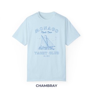 Peut inclure: Un t-shirt bleu clair avec un graphique de voilier et le texte "MONACO Monte Carlo YACHT CLUB Est 1953" en bleu.