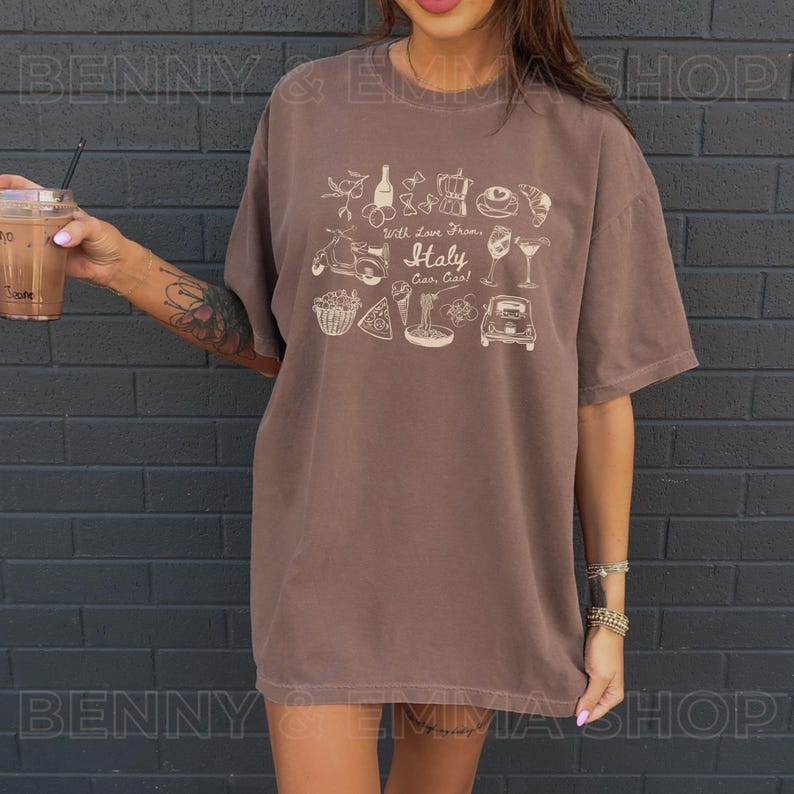 May include: An oversized brown t-shirt featuring a white graphic print of Italian-themed icons, including a Vespa scooter, pizza, pasta, wine glasses, and the text "With Love From Italy, Ciao!"